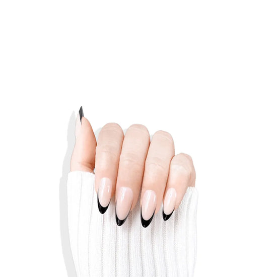 Claw pose showing de blinkie Midnight Frenchie soft nude base with black French tip press-on nails in short almond against a clean white background with a white ribbed knit sleeve