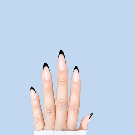Spread hand showing de blinkie Midnight Frenchie soft nude base with black French tip press-on nails in short almond against a soft blue background with a white ribbed knit sleeve
