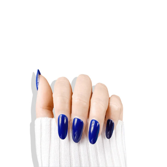 Downward claw pose showing de blinkie Midnight Reign cobalt blue gloss press-on nails in short oval against a white background with a white ribbed knit sleeve