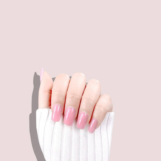 Claw pose showing de blinkie Miss Bubbleglam soft bubblegum pink press-on nails in short square against a soft pink background with a white ribbed knit sleeve