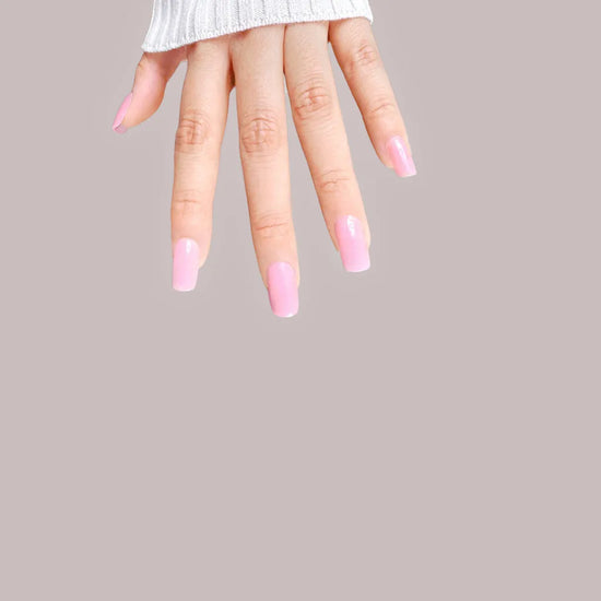 Downward spread hand showing de blinkie Miss Bubbleglam soft bubblegum pink press-on nails in short square against a soft mauve grey background with a white ribbed knit sleeve