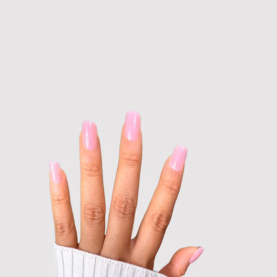 Spread hand showing de blinkie Miss Bubbleglam soft bubblegum pink press-on nails in short square against a soft light grey background with a white ribbed knit sleeve