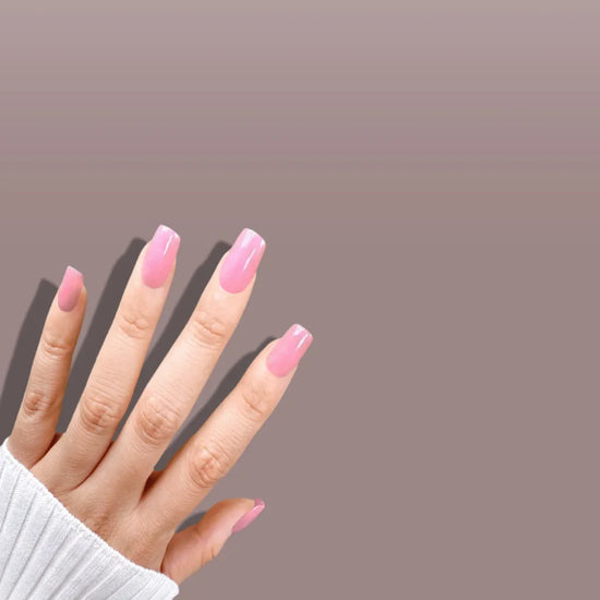Spread hand showing de blinkie Miss Bubbleglam soft bubblegum pink press-on nails in short square against a soft mauve grey background with a white ribbed knit sleeve