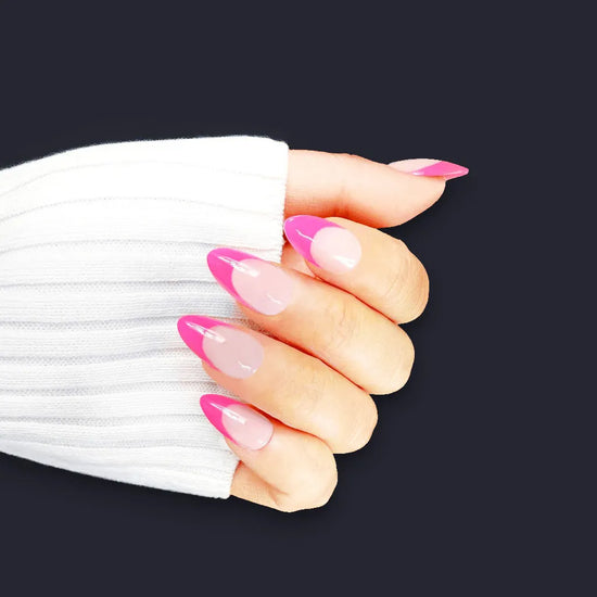 Claw pose showing de blinkie Miss Fuchsia Flick sheer nude base with electric pink curved French tip press-on nails in short almond shape against dark navy background with white ribbed sleeve
