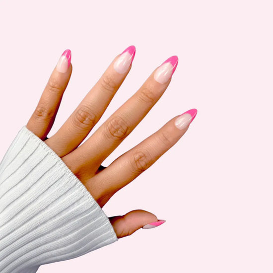 Spread hand showing de blinkie Miss Fuchsia Flick sheer nude base with electric pink curved French tip press-on nails in short almond shape against soft pink background with white ribbed sleeve