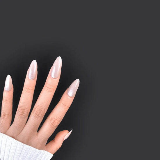 Spread hand showing de blinkie Miss Opaline velvet champagne nude press-on nails in short almond against a dark charcoal background with a white ribbed knit sleeve