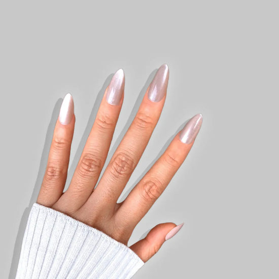 Full spread hand showing de blinkie Miss Opaline velvet champagne nude press-on nails in short almond against a soft light grey background with a white ribbed knit sleeve