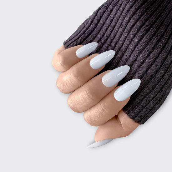 Claw downward pose showing de blinkie Miss Serene soft gloss milky white medium almond press-on nails against white background with dark knit sleeve