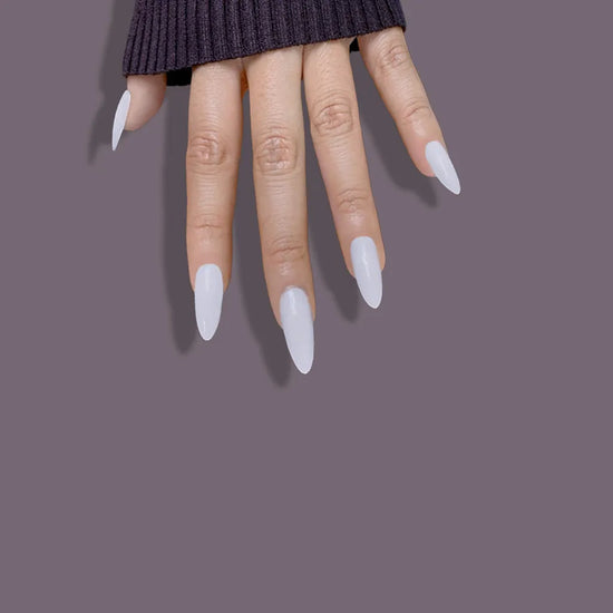 Fingers pointing down showing de blinkie Miss Serene soft milky white medium almond press-on nails against mauve background with dark knit sleeve