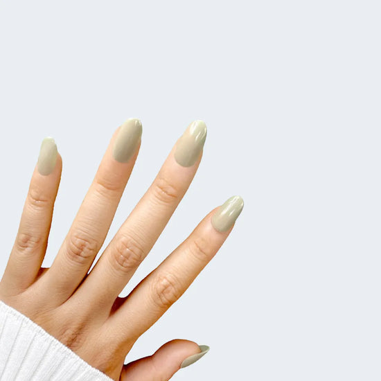 Spread hand pose showing de blinkie Olive Dusk muted olive grey press-on nails in short oval against a soft light grey background with a white ribbed knit sleeve