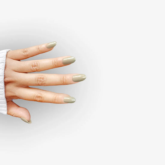 Spread hand lifestyle pose showing de blinkie Olive Dusk muted olive grey press-on nails in short oval against a white gradient background with a white ribbed knit sleeve