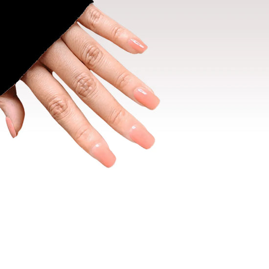 Side diagonal hand showing de blinkie Peach Glow soft peach nude jelly press-on nails in short square against a white background with a black sleeve