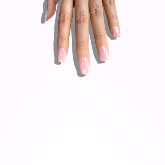 Fingers pointing downward showing de blinkie Pink Glimmer soft bubblegum pink glazed press-on nails in short square against a grey gradient background