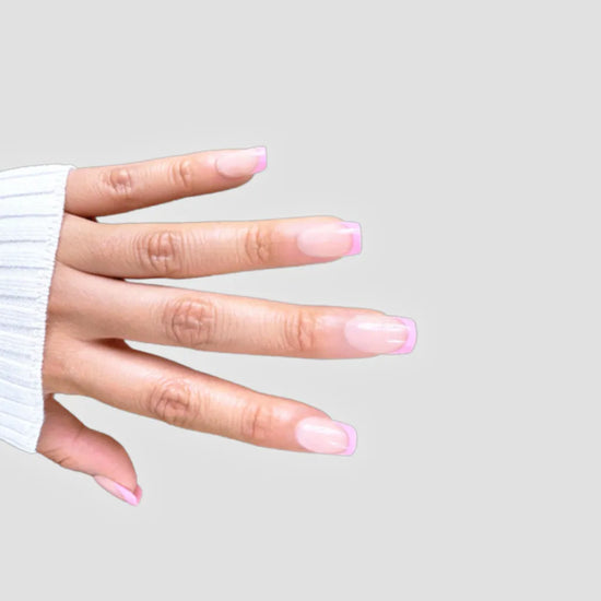 Horizontal spread hand showing de blinkie Pink Pop Frenchie sheer nude base with bubblegum pink French tip press-on nails in extra short square against a soft light grey background with a white ribbed knit sleeve