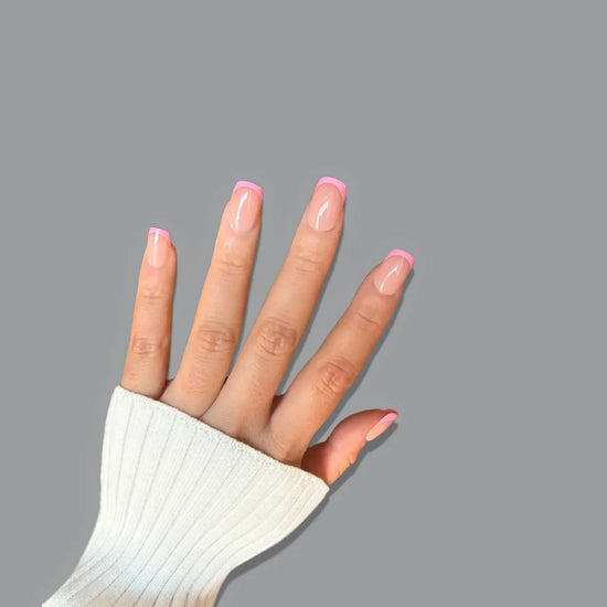 Upward spread hand showing de blinkie Pink Pop Frenchie sheer nude base with bubblegum pink French tip press-on nails in extra short square against a soft grey background with a white ribbed knit sleeve