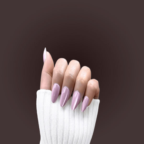 Claw pose showing de blinkie Princess Rosée soft lilac pink pearl press-on nails in short almond against a soft grey background with a white ribbed knit sleeve