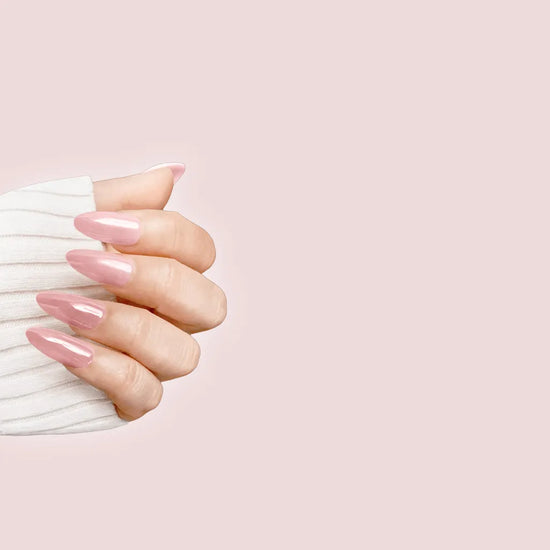 Claw pose showing de blinkie Rosé Glacé solid rose pink gloss press-on nails in medium almond against a soft blush pink background with a white knit sleeve