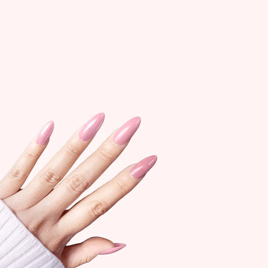 Diagonal upward hand showing de blinkie Rosé Glacé solid rose pink gloss press-on nails in medium almond against a soft blush pink background with a white ribbed knit sleeve