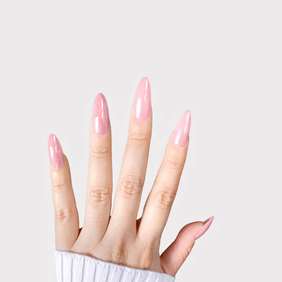 Fingers spread upward showing de blinkie Rosé Glacé solid rose pink gloss press-on nails in medium almond against a soft grey background with a white ribbed knit sleeve