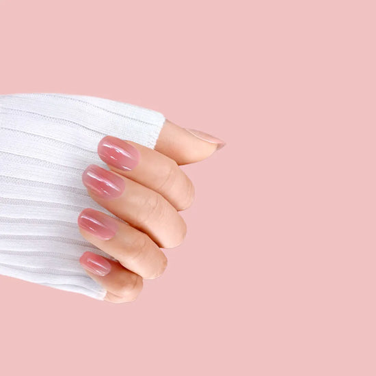 Claw pose showing de blinkie Rosé Jelly sheer warm rose ombre jelly press-on nails in extra short squoval shape against soft pink background with white ribbed sleeve