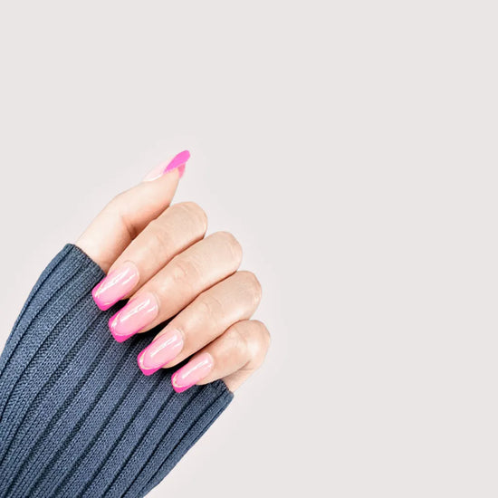 Claw pose showing de blinkie Rosé Mirage sheer blush pink with magenta French tips gold trace and 3D liner press-on nails in medium square shape against off-white background with denim knit sleeve