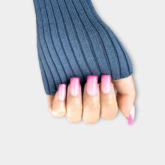 Upward claw pose showing de blinkie Rosé Mirage sheer blush pink with magenta French tips gold trace and 3D liner press-on nails in medium square shape against grey background with denim knit sleeve