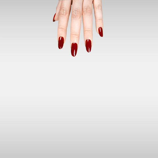 Fingers down pose showing de blinkie Royal Berry deep cherry red gloss press-on nails in short oval against a grey background with a white ribbed knit sleeve