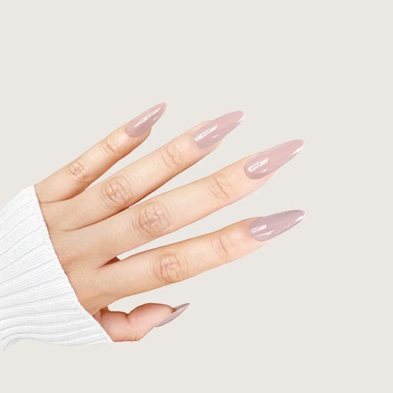Diagonal spread hand showing de blinkie Silken Mocha warm taupe nude press-on nails in medium almond against a warm cream background with a white ribbed knit sleeve