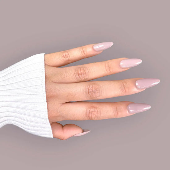 Side hand pose showing de blinkie Silken Mocha warm taupe nude press-on nails in medium almond against a soft mauve grey background with a white ribbed knit sleeve