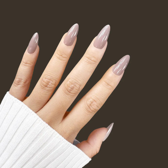 Spread hand pose showing de blinkie Silken Mocha warm taupe nude press-on nails in medium almond against a deep dark brown background with a white ribbed knit sleeve