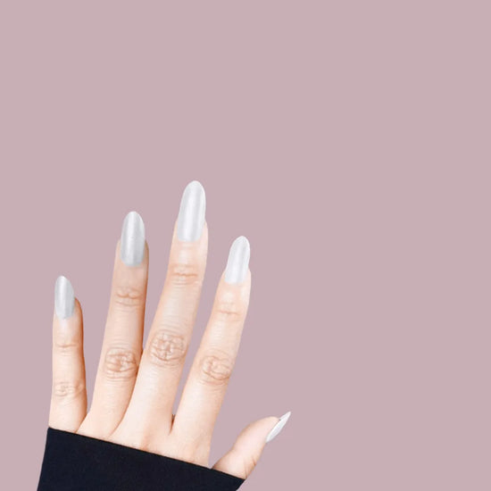Fingers spread pose showing de blinkie Silver Glint pearl white pearlescent press-on nails in short almond shape against mauve background with black sleeve