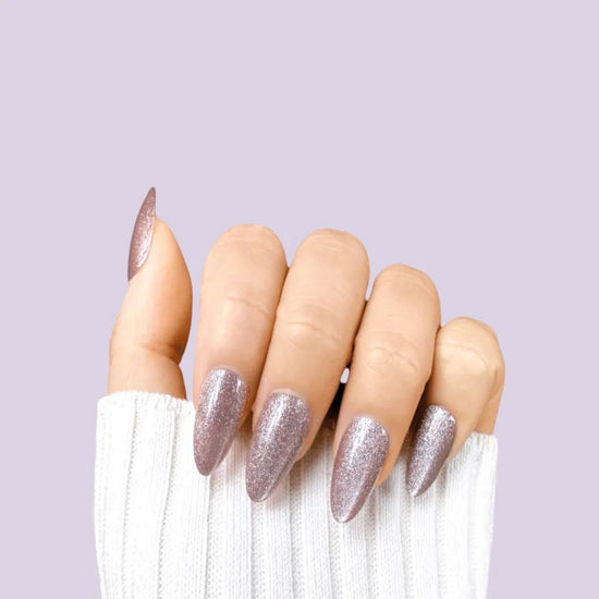 Starlight Sofia short almond press-on nails in dusty rose pink with fine silver-white shimmer, claw pose against lavender background with white knit sleeve