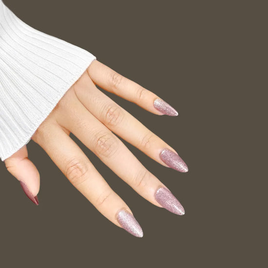 Fingers pointing down showing Starlight Sofia full-coverage silver-white shimmer dusty rose pink press-on nails in short almond shape, white sleeve and taupe background