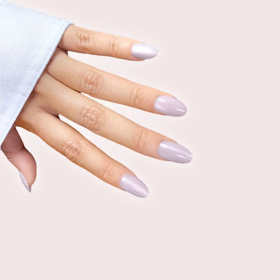 Downward hand showing Sugar Glaze pale lilac blush and silver shimmer short oval press-on nails against blush pink background with light blue sleeve