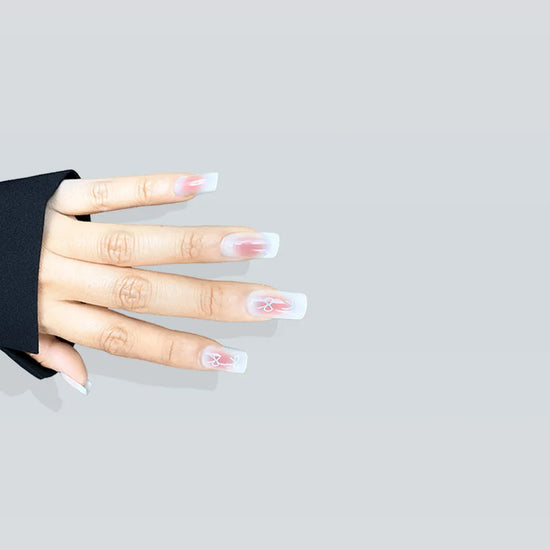 Spread hand showing de blinkie Sweetheart Tips rosy blush press-on nails with white bow nail art in short square shape against light grey background with black sleeve