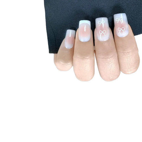 Downward claw pose showing de blinkie Sweetheart Tips rosy blush press-on nails with white heart and bow nail art in short square shape against white background with black sleeve