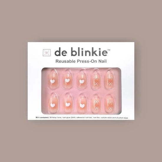 de blinkie Sweetheart Tips reusable press-on nail kit box showing 10 short square false nails with rosy blush centres and white heart and bow nail art on pink tray against warm taupe background