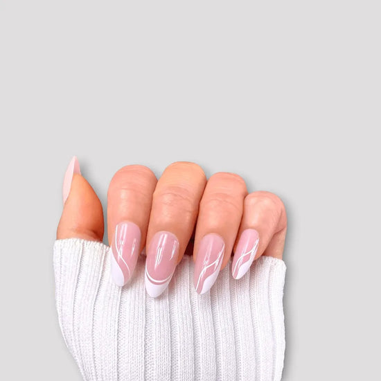 Claw pose showing de blinkie Swirl Baddie sheer pink base with white French tip and swirl nail art press-on nails in medium almond against a soft grey background with a white ribbed knit sleeve
