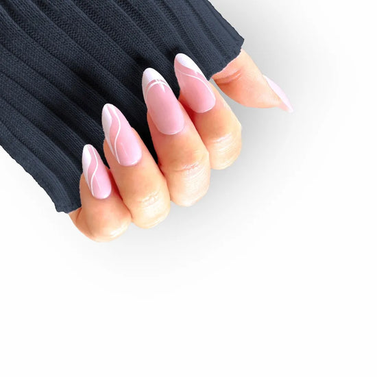 Upward claw pose showing de blinkie Swirl Baddie sheer pink base with white French tip and swirl nail art press-on nails in medium almond against a dark navy background with a dark ribbed knit sleeve