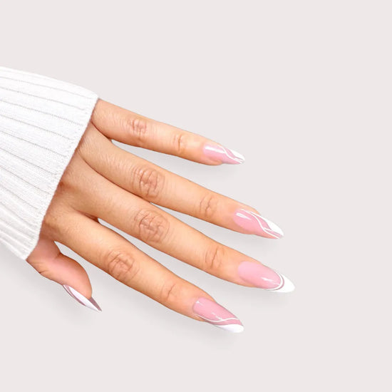 Diagonal downward spread hand showing de blinkie Swirl Baddie sheer pink base with white French tip and swirl nail art press-on nails in medium almond against a soft cream background with a white ribbed knit sleeve