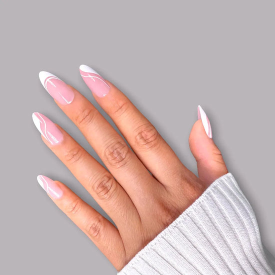 Diagonal spread hand showing de blinkie Swirl Baddie sheer pink base with white French tip and swirl nail art press-on nails in medium almond against a soft grey background with a white ribbed knit sleeve