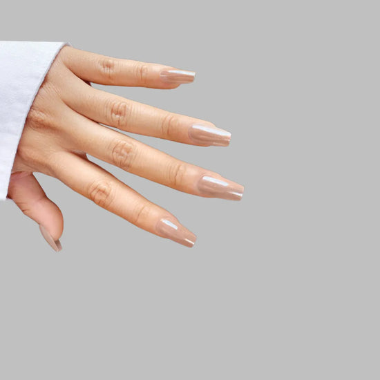Down-facing hand pose showing de blinkie The Executive Nude warm beige nude press-on nails in short coffin shape against light grey background with white sleeve