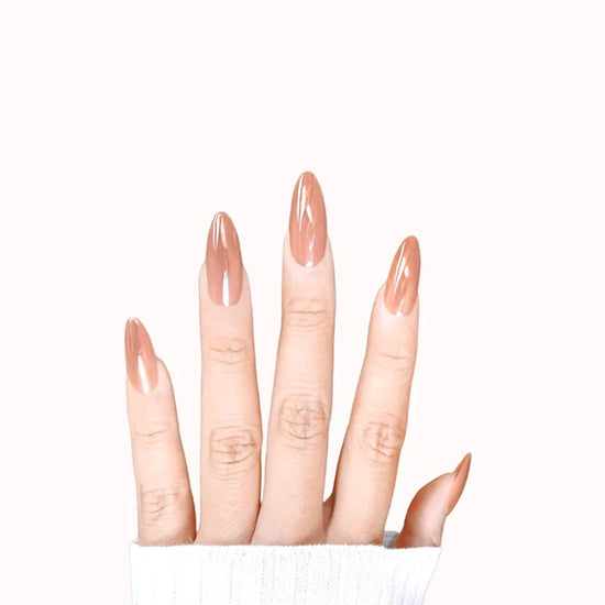 Fingers spread downward showing de blinkie Toffee Glazed warm caramel glazed gloss press-on nails in medium almond against a soft blush white background with a white ribbed knit sleeve