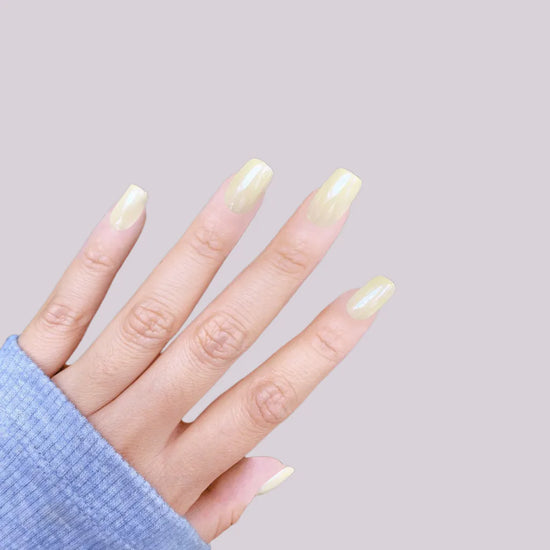 Fingers pointing upward showing Vanilla Crème butter yellow cream soft gloss short square press-on nails against lavender background with blue sleeve