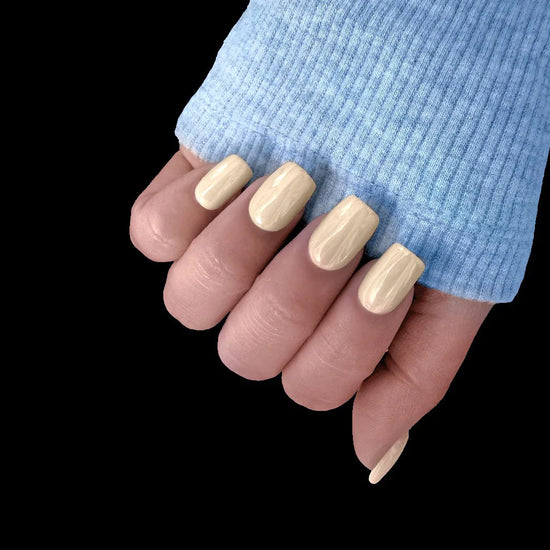 Fingers pointing down showing Vanilla Crème butter yellow cream short square press-on nails with blue sleeve against black background