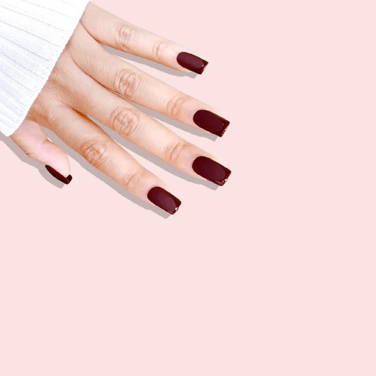 Fingers down pose showing de blinkie Velvet Bordeaux dark chocolate cherry velvet matte press-on nails in medium square shape against pink background with white ribbed knit sleeve