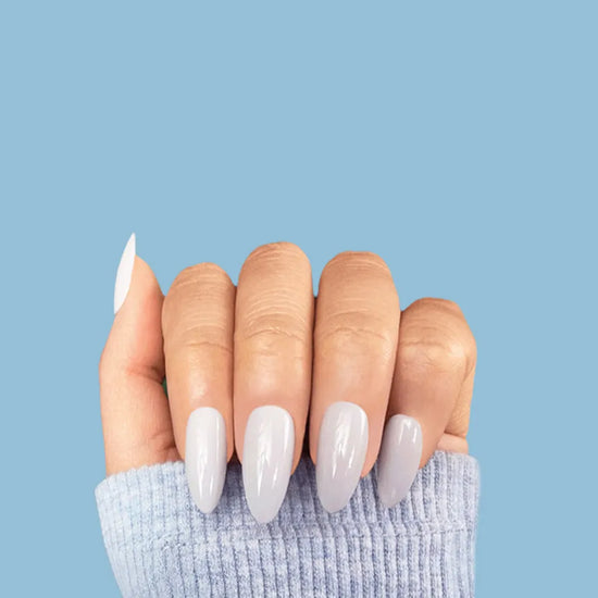 De Blinkie Lady Jane milky grey press on nails worn on hand against blue background - Almond shape, cool-toned minimalist design